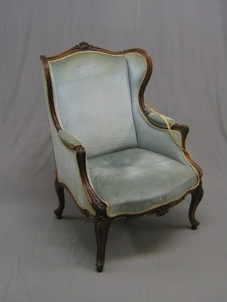 A late Victorian carved walnut show frame wing back chair, upholstered in blue material and raised on French cabriole supports