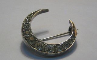 A silver crescent shaped brooch set white stones