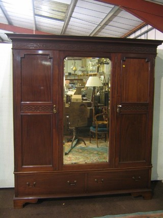 An Edwardian mahogany triple wardrobe with moulded cornice and blind fret work frieze, enclosed by an arched plate mirror panelled door, flanked by a pair of panelled doors, the base fitted 2 drawers, raised on bracket feet 79" wide