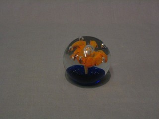 A circular glass paperweight with blue base set flowers and bubbles 3"