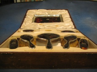 An 8 piece tortoiseshell and silver backed dressing table set, comprising tray, hand mirror, pair of clothes brushes, pair of hair brushes, pair of cut glass dressing table jars and covers (comb and 1 other item missing), cased