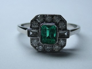 A lady's 18ct white gold dress ring set a rectangular cut emerald the shoulders set 2 baguette cut diamonds supported by numerous diamonds (0.40/0.52ct)