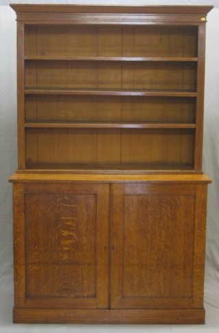 An oak bookcase on cabinet, the upper section with moulded cornice fitted adjustable shelves, the base fitted a double cupboard enclosed by panelled doors, raised on a platform base 48"