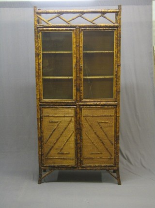 A 1930's bamboo display cabinet, the upper section fitted shelves enclosed by glazed panelled doors, the base fitted shelves enclosed by panelled doors, 35"