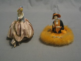 A 1920's porcelain powder puff with porcelain head in the form of a seated bonnetted lady (bonnet f) and a do. pin cushion