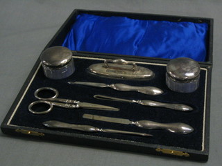 An 8 piece silver plated manicure set with 2 circular cut glass jars with plated lids, do. buffer, pair of scissors, nail file and 2 other items, cased