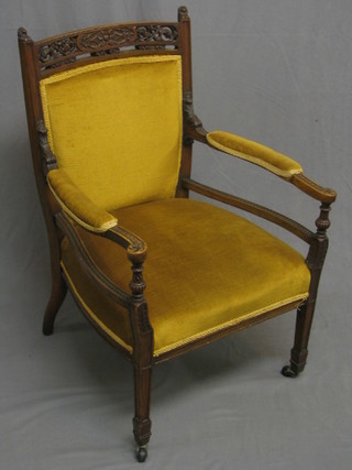An Edwardian walnut open arm chair with pierced and carved cresting rail and upholstered seat and back
