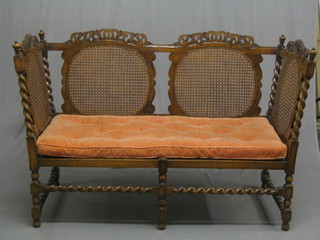 A 1930's pierced and carved oak Carolean style sofa with woven cane back, raised on spiral turned supports 58"