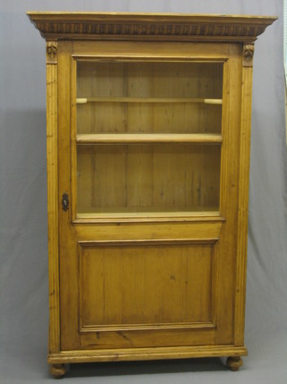 A 19th Century French stripped pine cabinet with moulded cornice, the interior fitted shelves enclosed by a glazed panelled door, raised on bun feet 42"