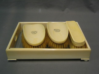 An Art Deco glass and ivory dressing table tray, raised on bun feet (1 missing), a pair of military ivory backed hair brushes and a clothes brush