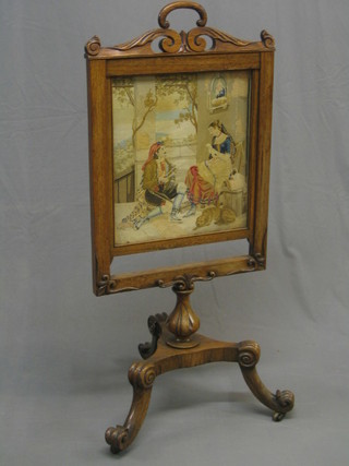 A Victorian carved rosewood fire screen with Berlin wool work panel depicting a wool winding scene, raised on a triform base with scrolled feet 22" (old repair to handle on top)