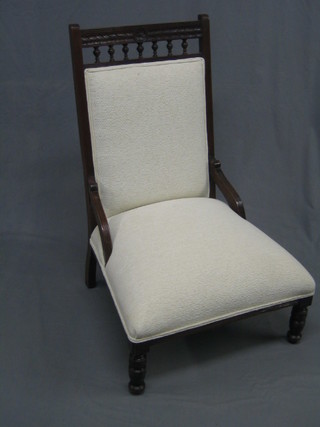 An Edwardian mahogany nursing chair upholstered in white material and raised on turned supports