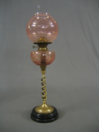 A Victorian pink glass oil lamp reservoir and shade raised on a spiral turned column with black socle base