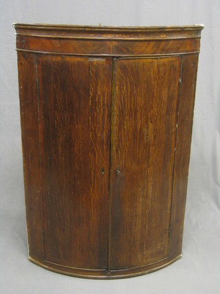 A Georgian Country oak and mahogany bow front corner cabinet with moulded cornice, the interior fitted shelves enclosed by panelled doors (left hand panel split) 29"