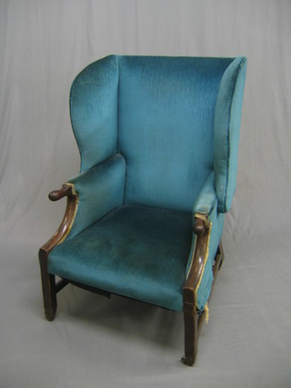 A 19th Century mahogany framed wing armchair, upholstered in blue material, raised on square tapering supports ending in brass caps and castors