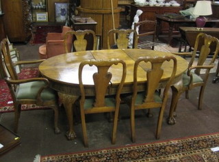 A 1950's Queen Anne style figured walnut dining suite comprising oval extending dining table with 1 extra leaf and a 6 Queen Anne style splat back dining chairs (2 carvers, 4 standard), all raised on cabriole supports 
