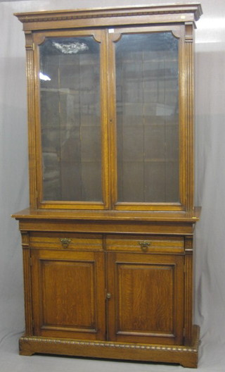 A Victorian oak bookcase on cabinet, the upper section with moulded cornice, the interior fitted adjustable shelves enclosed by glazed panelled doors, the base fitted 2 drawers above a double cupboard, raised on a platform base 48"