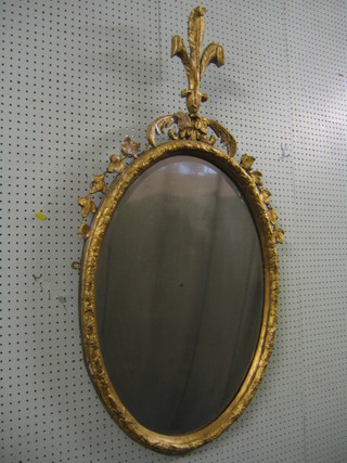 A 19th Century oval bevelled plate wall mirror contained in a decorative gilt frame surmounted by a fleur de lis, 31"