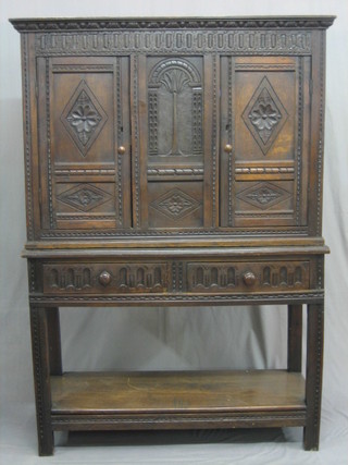 An 18th Century carved oak cabinet with moulded cornice and painted decoration, fitted 2 cupboards enclosed by panelled doors, raised on an associated later base fitted 2 drawers with potboard, 45"