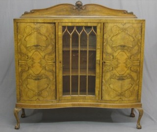 A 1930's Queen Anne style figured walnut display cabinet with carved raised back, fitted shelves enclosed by astragal glazed doors, flanked by a pair of bow front cupboards enclosed by panelled doors, raised on cabriole ball and claw supports 53"