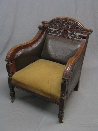 A Victorian carved mahogany show frame library chair, upholstered in brown rexine, raised on square supports ending in castors
