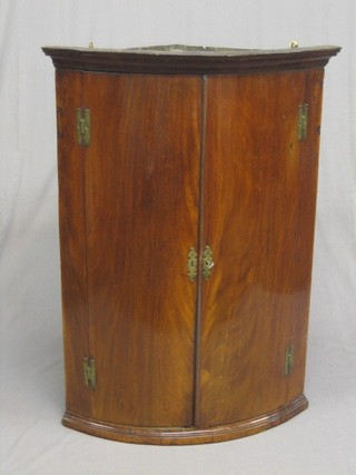 A Georgian mahogany bow front hanging corner cabinet with moulded cornice, the interior fitted shelves enclosed by panelled doors 30"