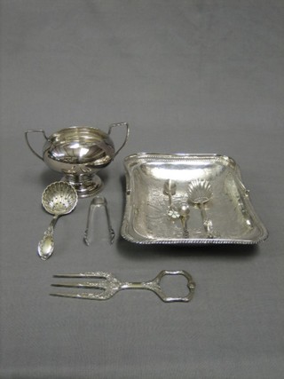 A silver plated bread fork, an engraved cake basket with swing handle, a twin handled sugar bowl, 4 plated spoons and a pair of sugar tongs