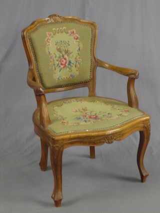 A 20th Century French carved walnut open arm salon chair with Berlin wool work back and seat, raised on cabriole supports