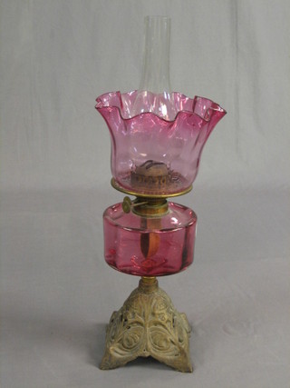 A cranberry glass oil lamp reservoir raised on a pierced gilt metal stand complete with shade (chipped)