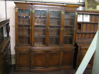 An Edwardian oak break front triple bookcase with moulded cornice and carved arcaded decoration, the interior fitted adjustable shelves enclosed by astragal glazed doors, the base fitted a brushing slide above triple cupboards, raised on a platform base 72"