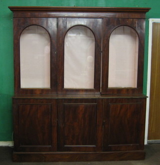 A large Victorian mahogany bookcase on cabinet, the upper section with moulded cornice enclosed by arch shaped panelled doors, the base fitted 3 long drawers enclosed by panelled doors, raised on a platform base 74"