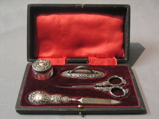 An Edwardian embossed silver 4 piece manicure set comprising buffer, rouge pot and cover, scissors and nail file, Birmingham 1903, cased
