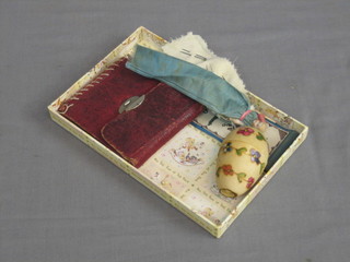 A sewing set contained in a leather case, a miniature porcelain doll topped needle case, a turned wooden bobbin egg