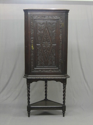 A Victorian heavily carved oak corner cabinet with moulded and dentil cornice, the shelved interior enclosed by a carved panelled door, raised on an associated stand with spiral turned supports 28"