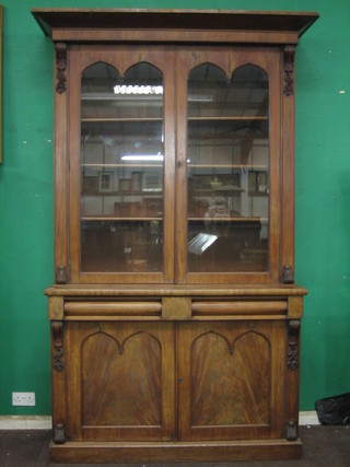 A Victorian mahogany bookcase on cabinet with moulded cornice, the interior fitted shelves enclosed by arched panelled doors, the base fitted 2 long drawers above a double cupboard enclosed by arched panelled doors, raised on a platform base 55 1/2"