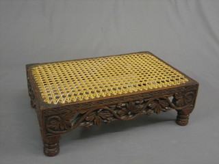 A pierced and carved oak footstool, raised on turned supports with woven cane seat 15"