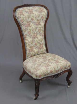 A Victorian carved walnut high backed show frame nursing chair upholstered in floral material raised on cabriole supports