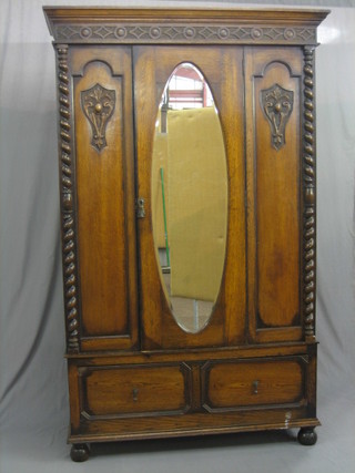 A 1930's oak Jacobean style wardrobe with carved and moulded cornice enclosed by an arched bevelled plate mirrored door, the base fitted a drawer with spiral turned column decoration to the sides, raised on bun feet (old worm to bun feet) 50"
