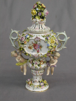 A Dresden style twin handled and floral encrusted urn and cover decorated cherubs to the sides 7" (chips)