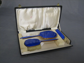 A gilt metal and blue enamelled 3 piece dressing table set with hand mirror, hair brush and clothes brush, cased