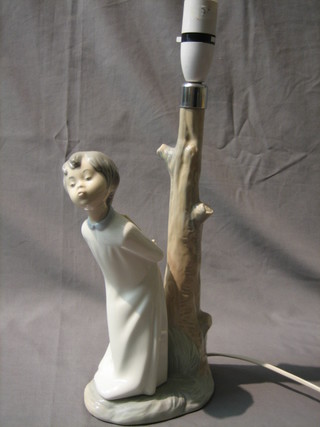 A Nao lamp base in the form of a standing child dressed in a night gown by a tree stump 13"