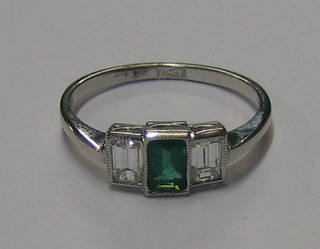 A lady's 18ct white gold dress ring set a rectangular cut emerald supported by 2 diamonds