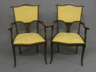 A pair of Edwardian inlaid mahogany open arm chairs, the seats of serpentine outline and upholstered in yellow material, raised on cabriole supports