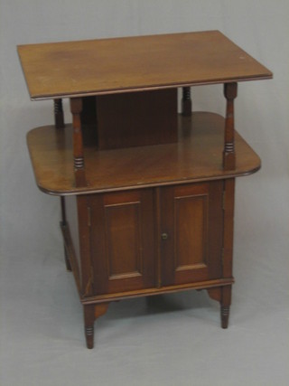 An Edwardian square 2 tier book table enclosed by a panelled door raised on turned and block supports 24"
