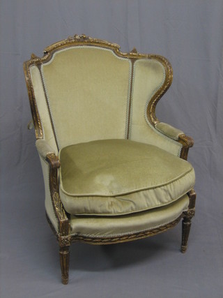A French Edwardian carved gilt open wing back chair upholstered in green material, raised on turned and fluted supports