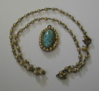 An oval turquoise pendant surrounded by simulated pearls hung on a simulated pearl chain