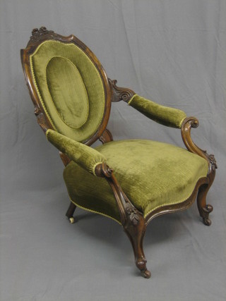A Victorian carved mahogany show frame spoon back open arm chair upholstered in green material, raised on cabriole supports