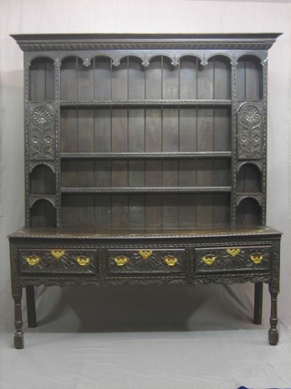 An 18th/19th Century carved oak dresser, the raised back with moulded and carved cornice and fitted 3 shelves flanked by a pair of cupboards with niches, the base fitted 3 long drawers, raised on turned and block supports 68"