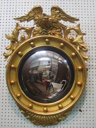 A handsome 19th Century convex plate wall mirror contained in a circular ball studded frame surmounted by a figure of an eagle, 27"