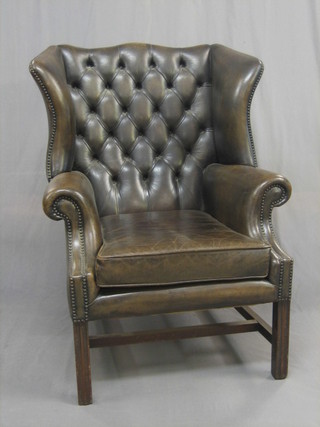 A Georgian style mahogany framed winged armchair upholstered in green buttoned leather